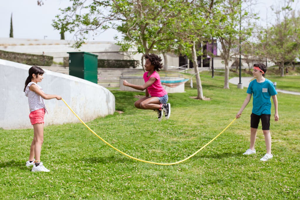 Children enjoying a sunny day playing jump rope outdoors in a park.
