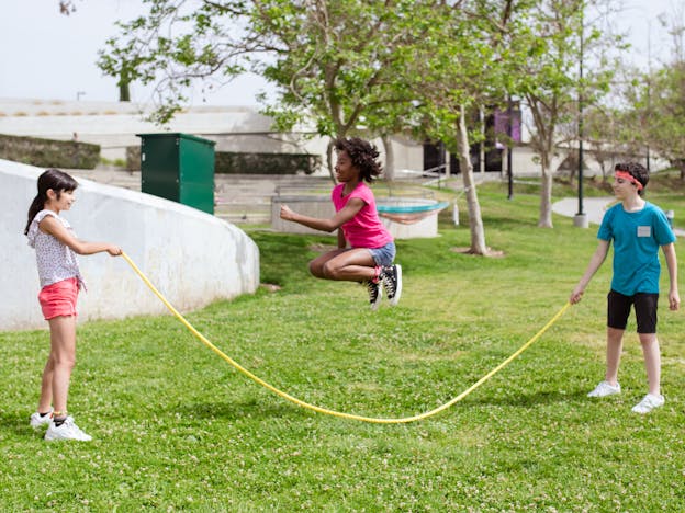 Children enjoying a sunny day playing jump rope outdoors in a park.