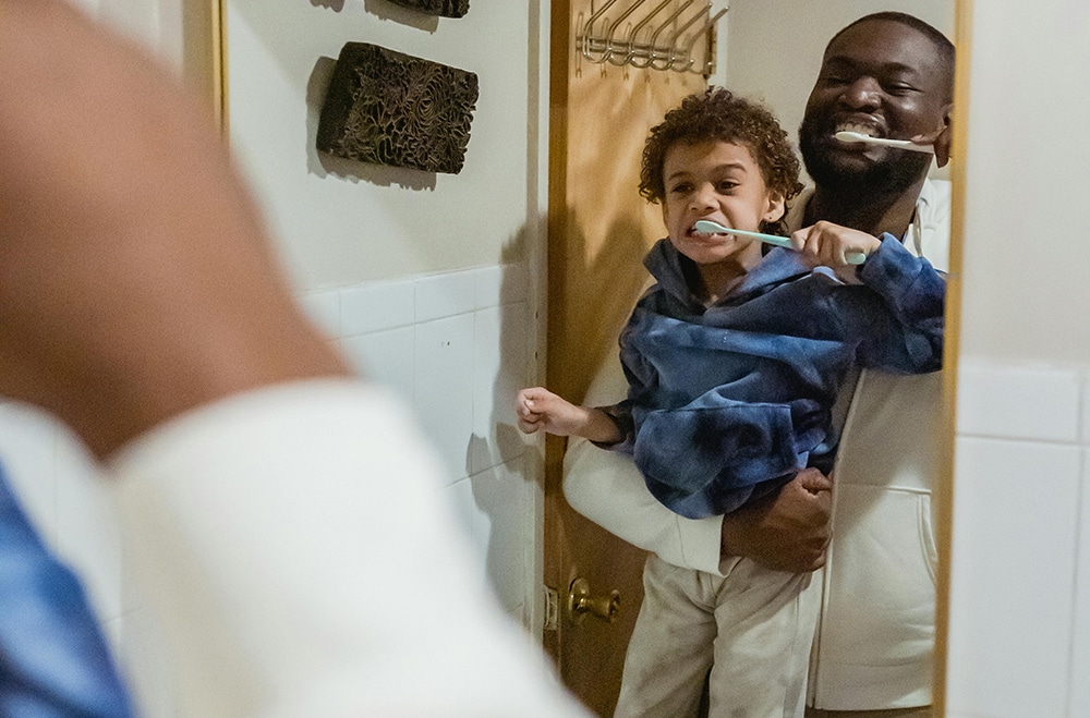 Dental Health month. Man brushing his teeth with his son. 